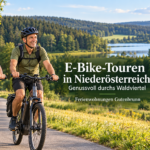 ebike touren niederösterreicher anna und herbert - Ferienwohnungen Gutenbrunn Banner of two seniors biking on a sunny trail by a lake and forest; headline promotes E-Bike-Touren in Niederösterreich with Anna & Herbert photo.