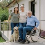 barrierefreie-unterkunft-mit-garten-finden-1790487989 - Ferienwohnungen Gutenbrunn Smiling family of three with a golden retriever posing outside a modern home; a man in a wheelchair sits beside them.