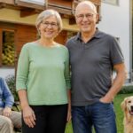 vacation-rental-gutenbrunn-your-getaway-in-the-Waldviertel-1791614634-7 - Vacation Rentals in Gutenbrunn A happy family posing in a sunny front yard: a man in a wheelchair, his partner behind him, an older couple beside them, and a golden retriever nearby.