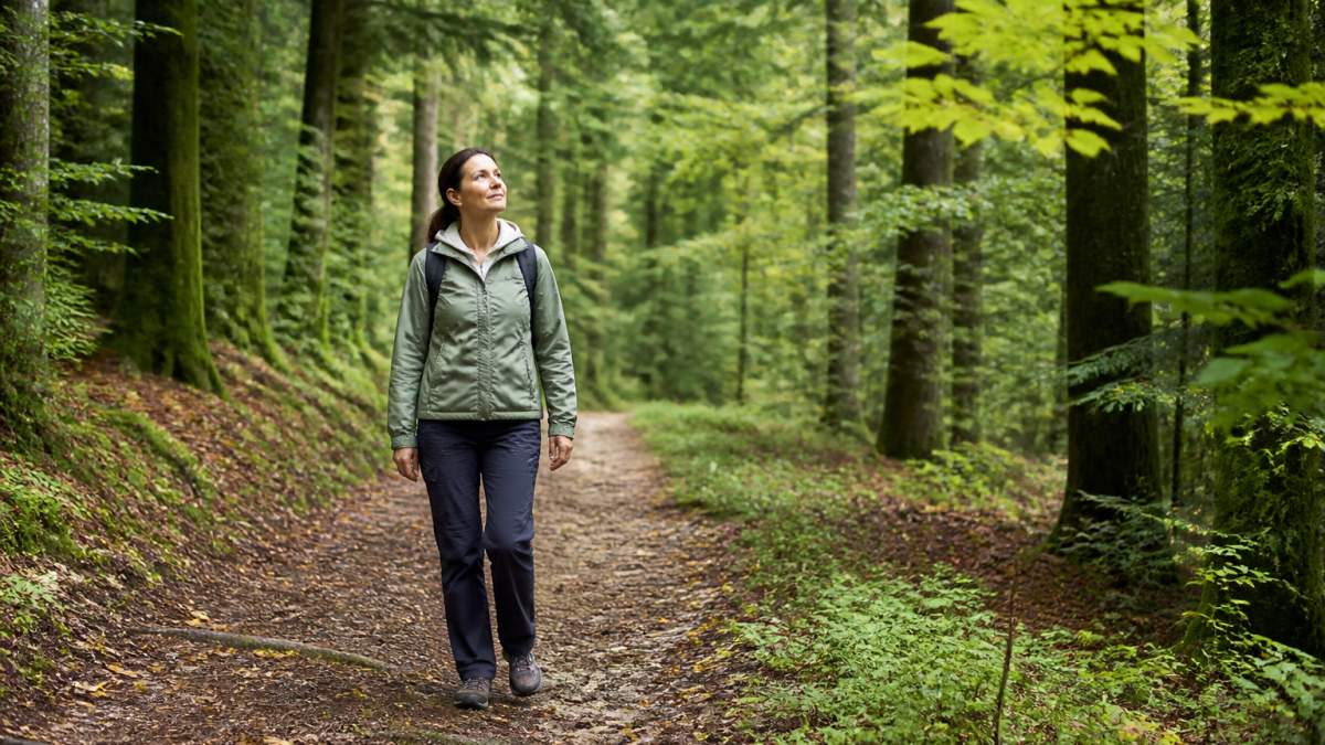 Person beim entspannten Spaziergang auf einem Waldweg im Waldviertel, umgeben von grünen Bäumen und ruhiger Natur bei diffusem Tageslicht